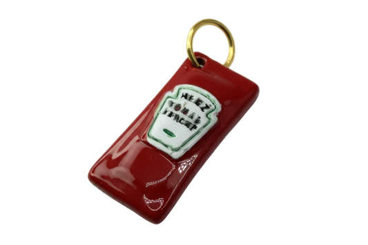 Glossy red ketchup bottle charm with raised white label, green outline, and gold top