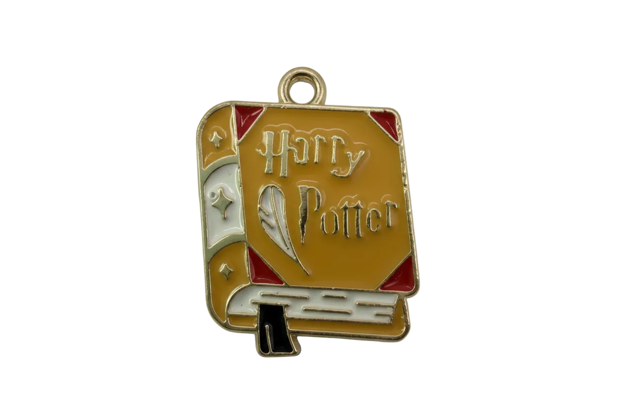 Gold-toned enamel spellbook charm in mustard yellow with red corners, white spine, and quill detail