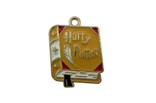 Gold-toned enamel spellbook charm in mustard yellow with red corners, white spine, and quill detail