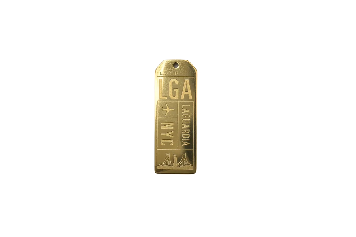 Gold engraved rectangular travel tag with airplane icon, stacked letters, and skyline detail