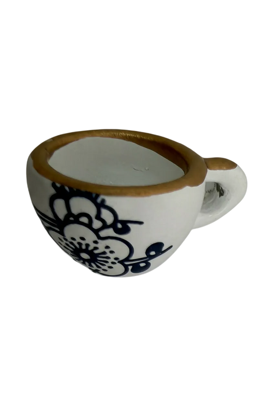 White oval piece with black lace floral design and gold edge, angled side view