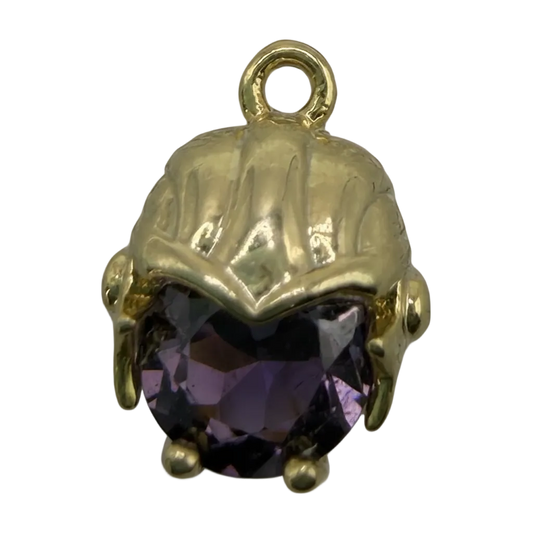 Polished gold scallop shell with a faceted deep purple gem, close-up on black background