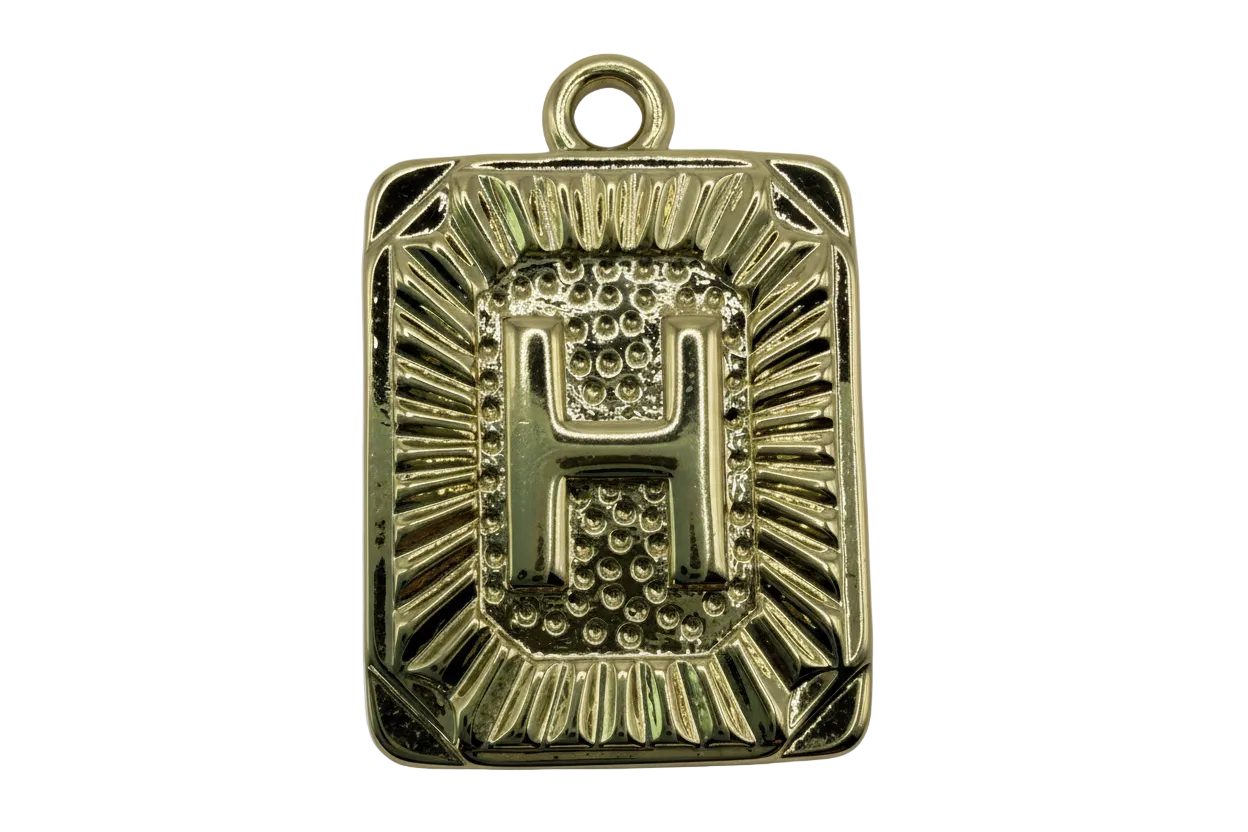 Gold rectangular initial tag with raised letter H and textured sunburst border