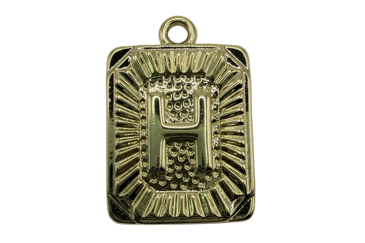Gold rectangular initial tag with raised letter H and textured sunburst border