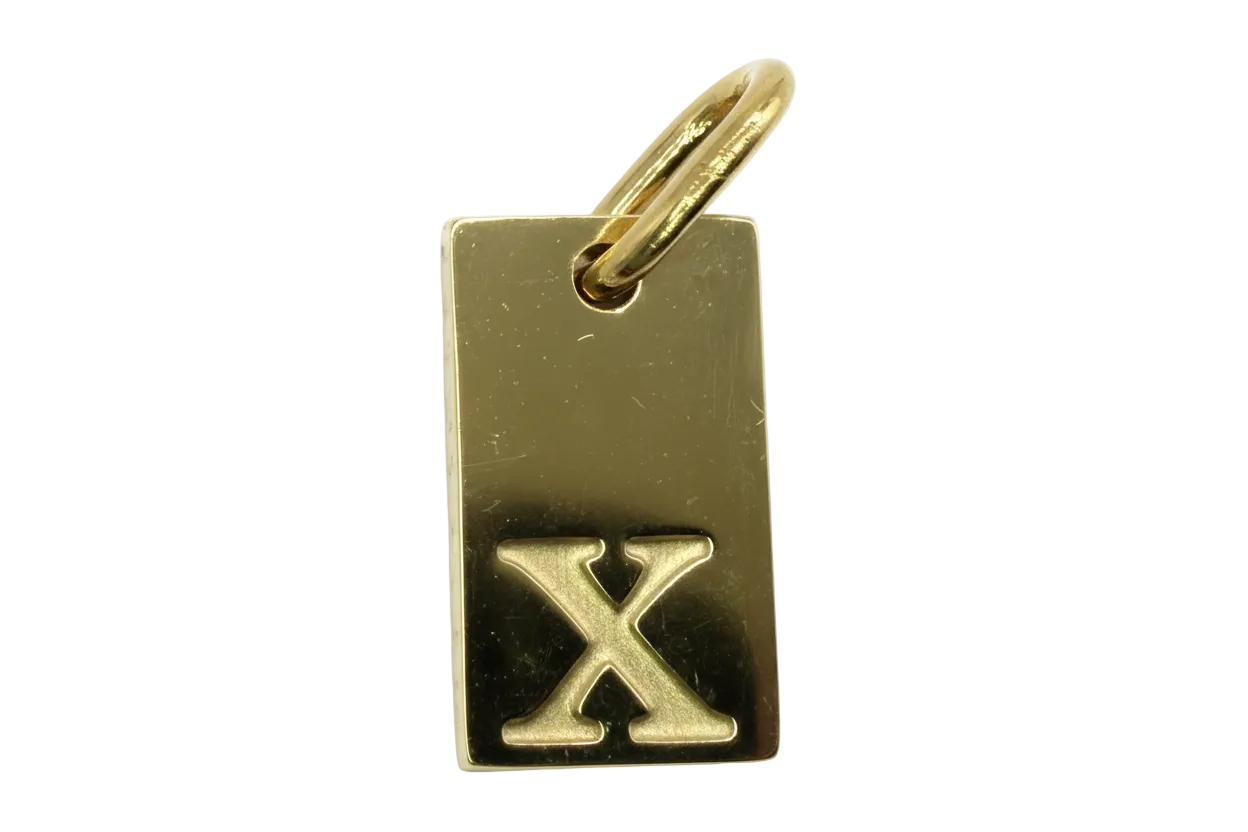 Gold rectangular tag with raised letter X on a polished surface
