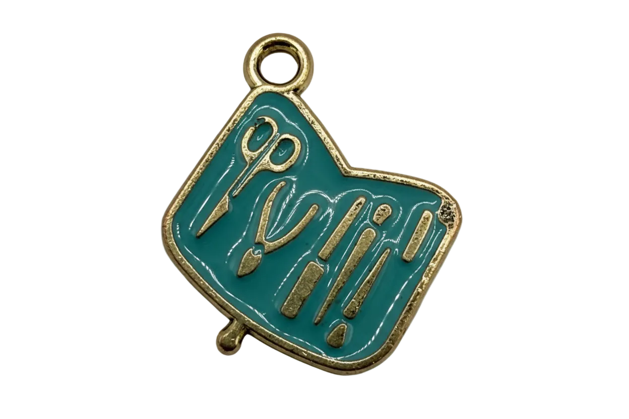 Teal enamel art tools plaque with gold outline and raised scissors, brush, and pencil details