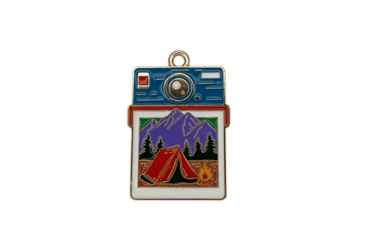 Gold-trimmed enamel instant camera with mountain camping photo, red tent, pine trees, and campfire