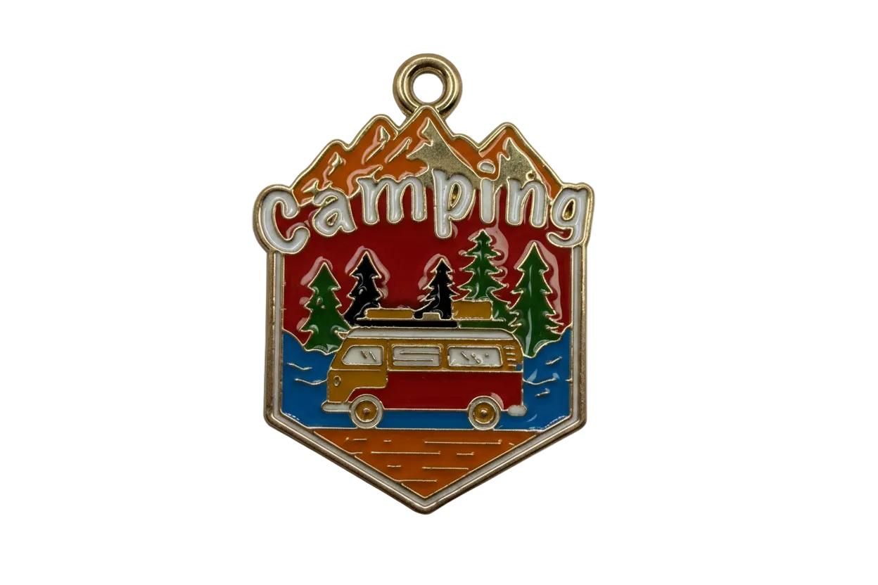 Gold-tone enamel camping badge with mountains, pine trees, and a retro camper van in red, blue, and green