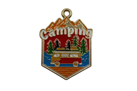 Gold-tone enamel camping badge with mountains, pine trees, and a retro camper van in red, blue, and green