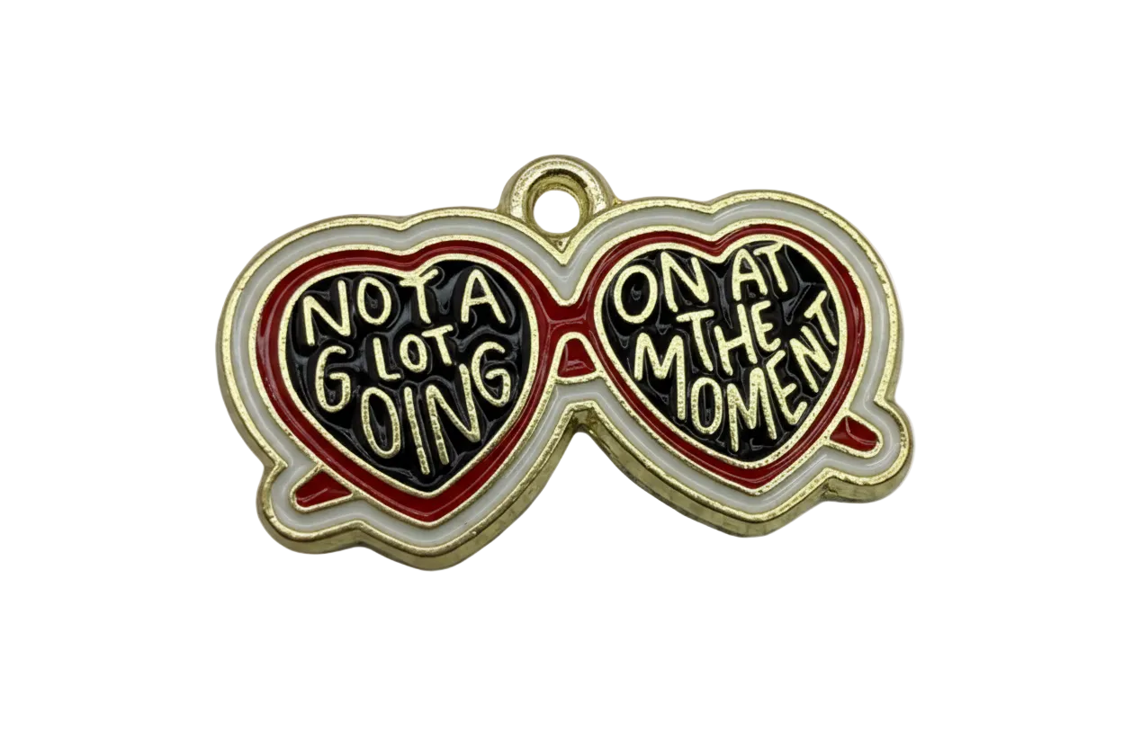 Gold-finished heart-shaped sunglasses charm with black enamel lenses, red and white frame, and raised quote lettering