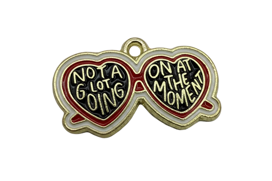Gold-finished heart-shaped sunglasses charm with black enamel lenses, red and white frame, and raised quote lettering