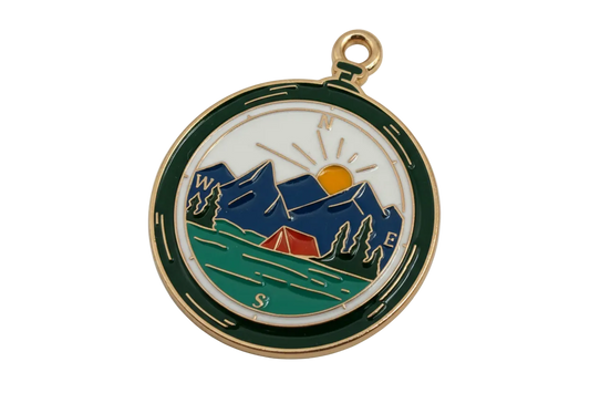 Round gold enamel compass medallion with mountains, sunrise, lake, trees, and a red tent