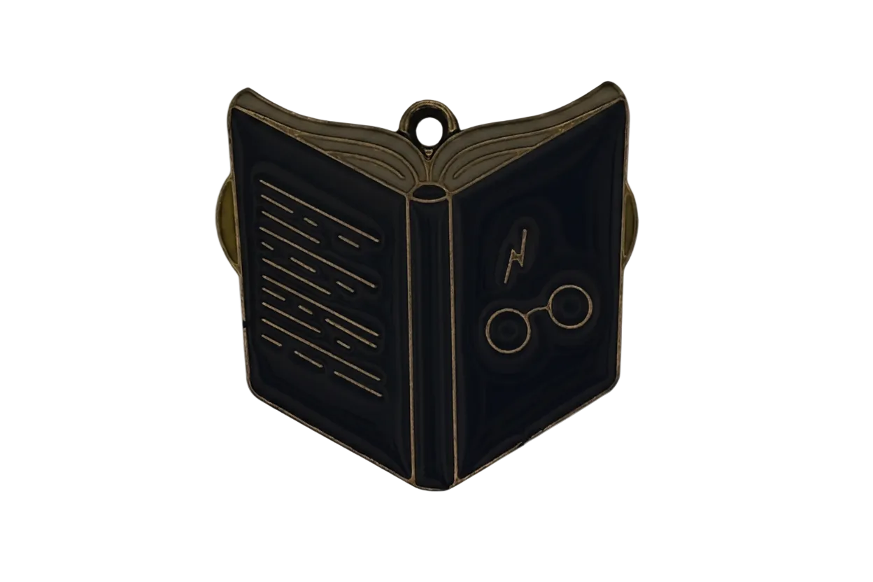 Close-up of a black enamel open book charm with gold outlines, showing a lightning bolt and round glasses.