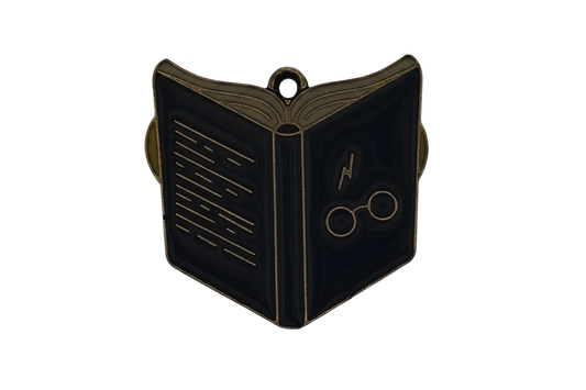 Close-up of a black enamel open book charm with gold outlines, showing a lightning bolt and round glasses.