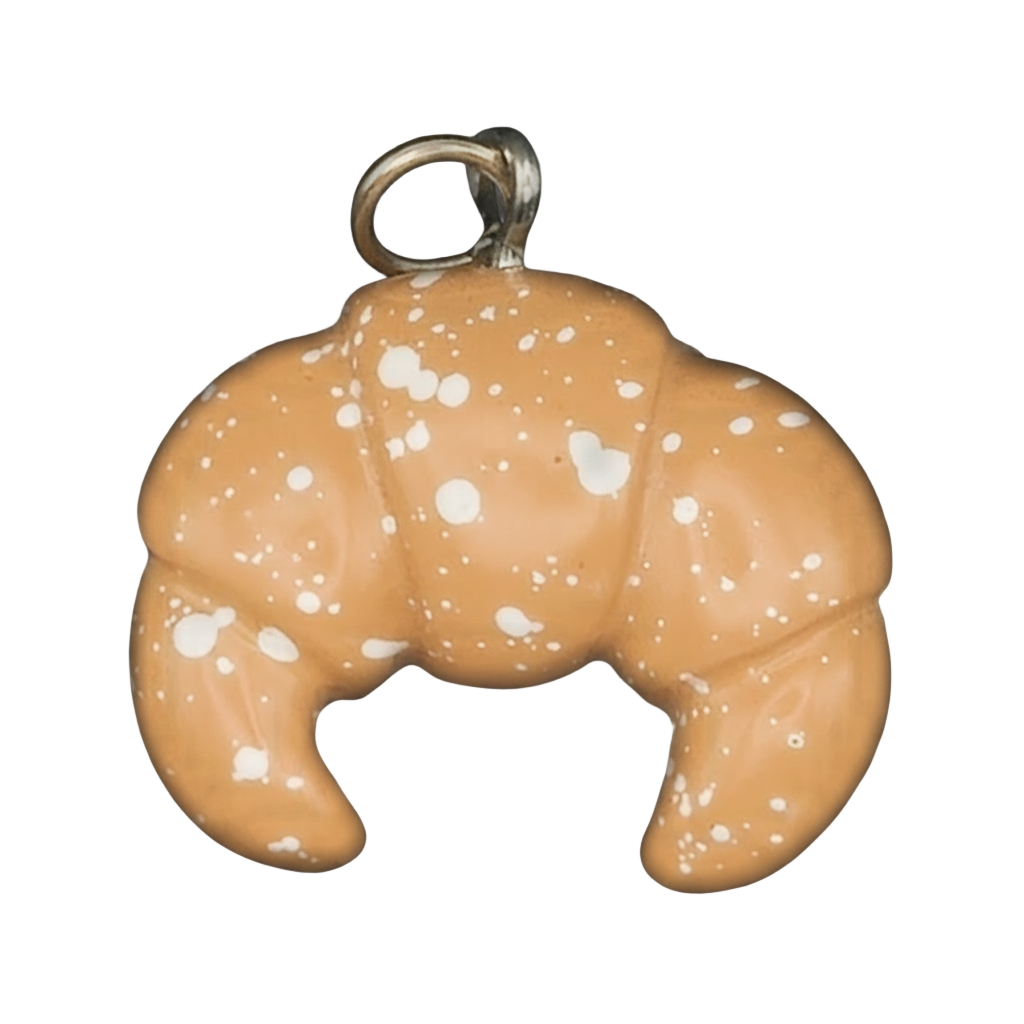 Close-up of tan croissant-shaped enamel charm with white speckles on black background.