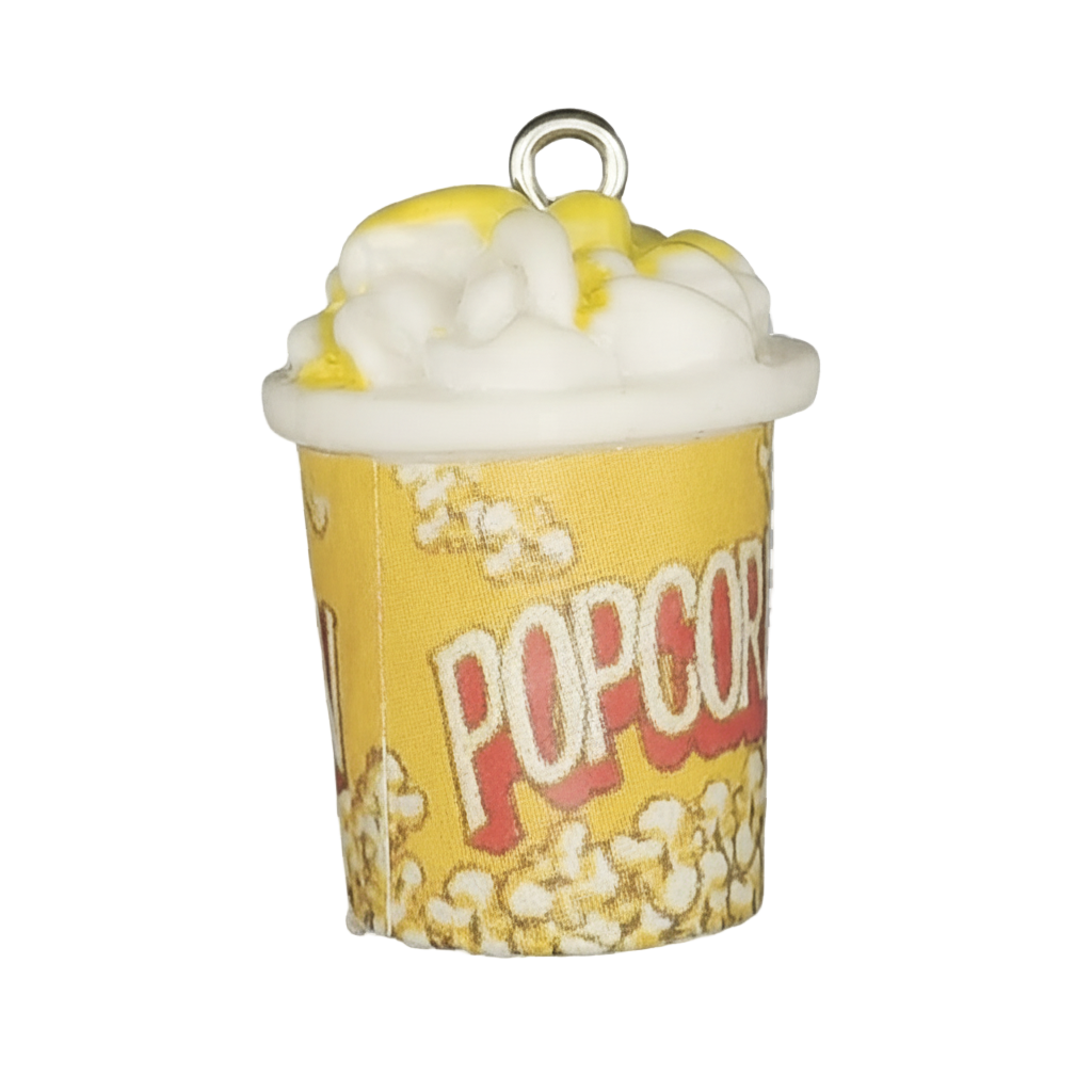 Close-up of a yellow POPCORN bucket charm topped with white popcorn and yellow butter on a black background.
