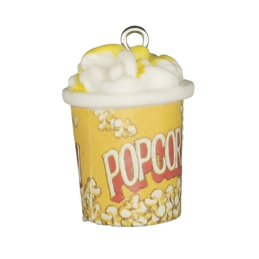 Close-up of a yellow POPCORN bucket charm topped with white popcorn and yellow butter on a black background.