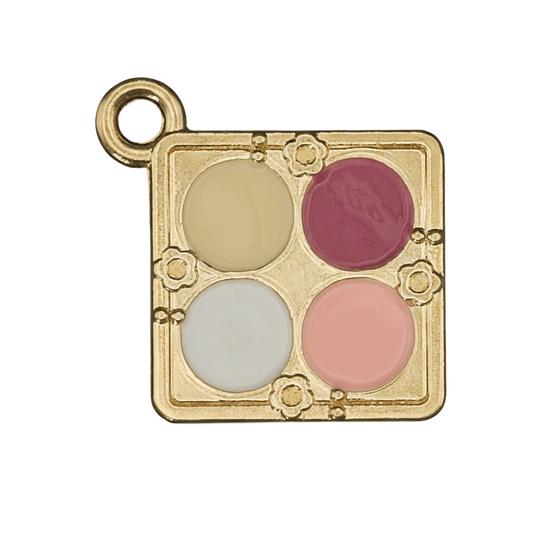 close-up of gold-tone square charm shaped like a four-color makeup palette with yellow, dark pink, white, and peach enamel on black background