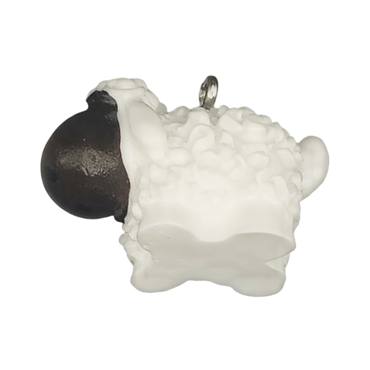 close-up of small white sheep charm with black head on a black background