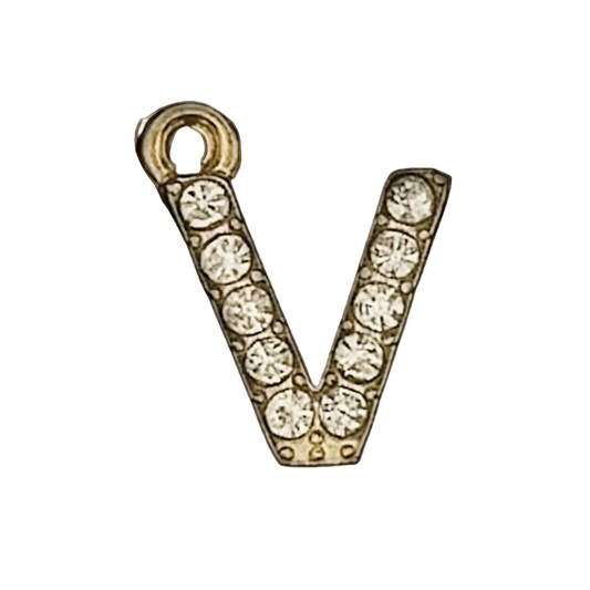 close-up of a gold-tone letter V charm with clear crystals on a black background