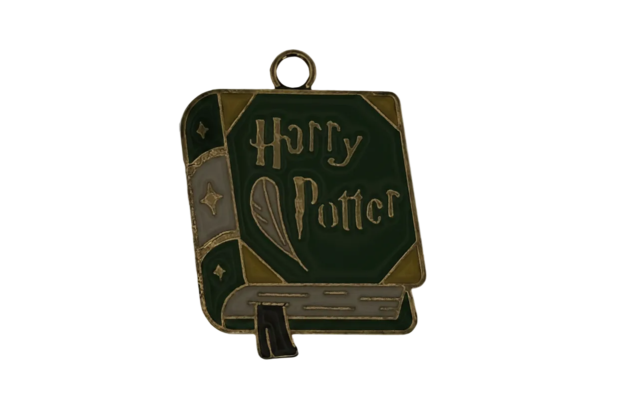Close-up of a green enamel book-shaped charm with gold-tone outline and a quill design on the cover, on a black background.