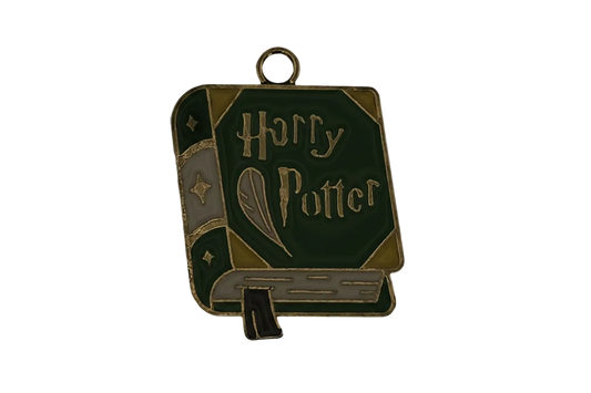 Close-up of a green enamel book-shaped charm with gold-tone outline and a quill design on the cover, on a black background.