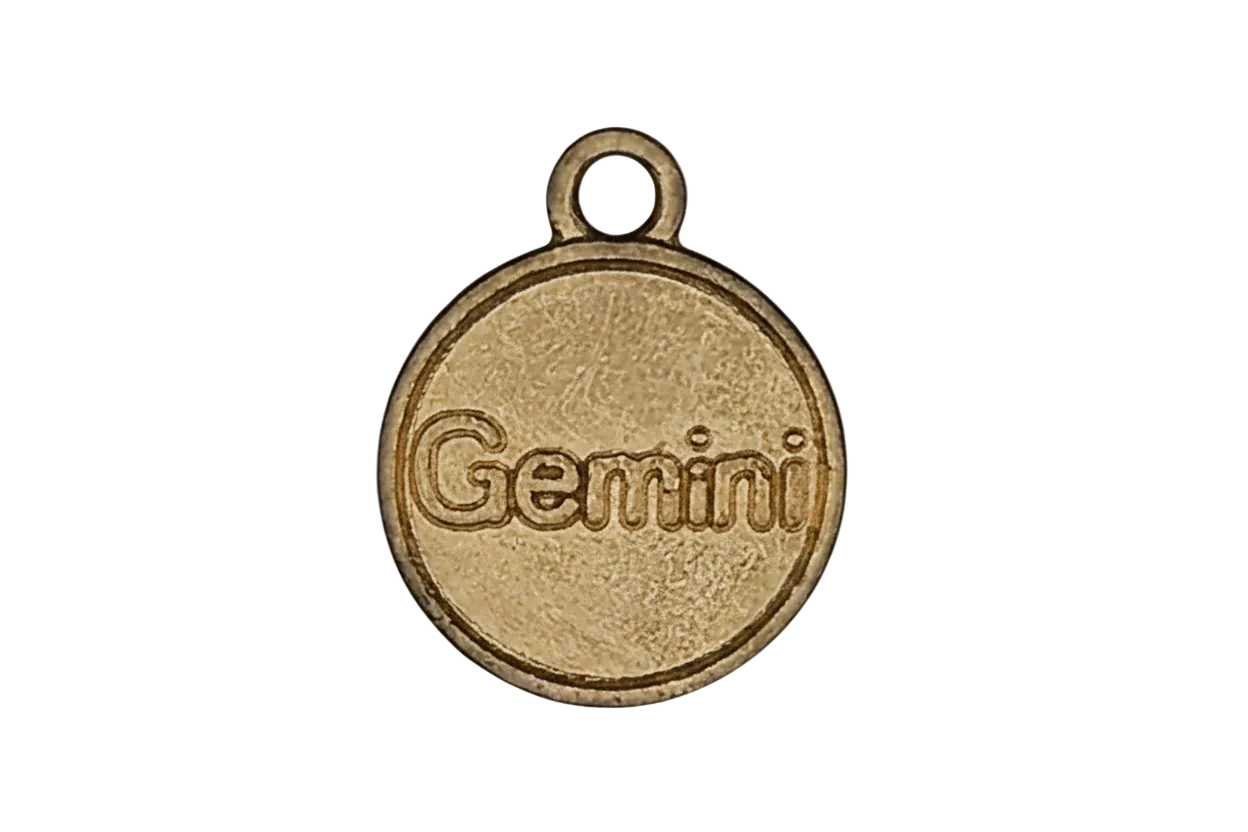 close-up of gold-tone round charm with the word Gemini on black background
