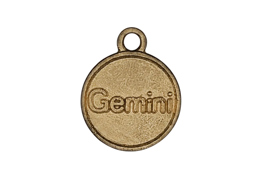 close-up of gold-tone round charm with the word Gemini on black background