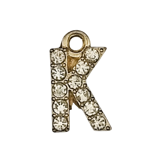 close-up of gold-tone letter K charm with clear crystals on black background