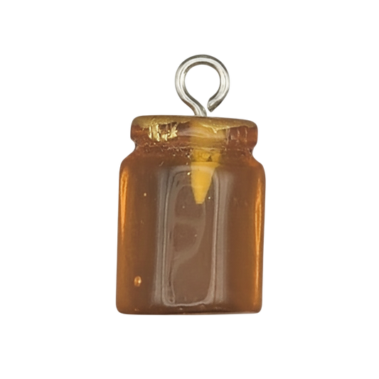 close-up of a miniature honey jar charm with amber fill on a black background