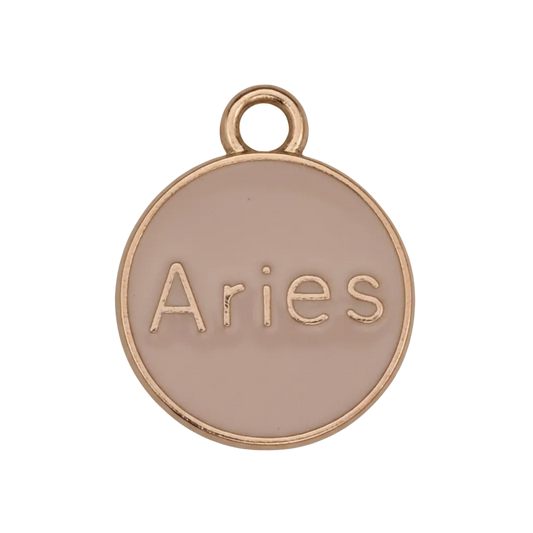 close-up of round pink enamel charm with gold edge reading Aries on a black background