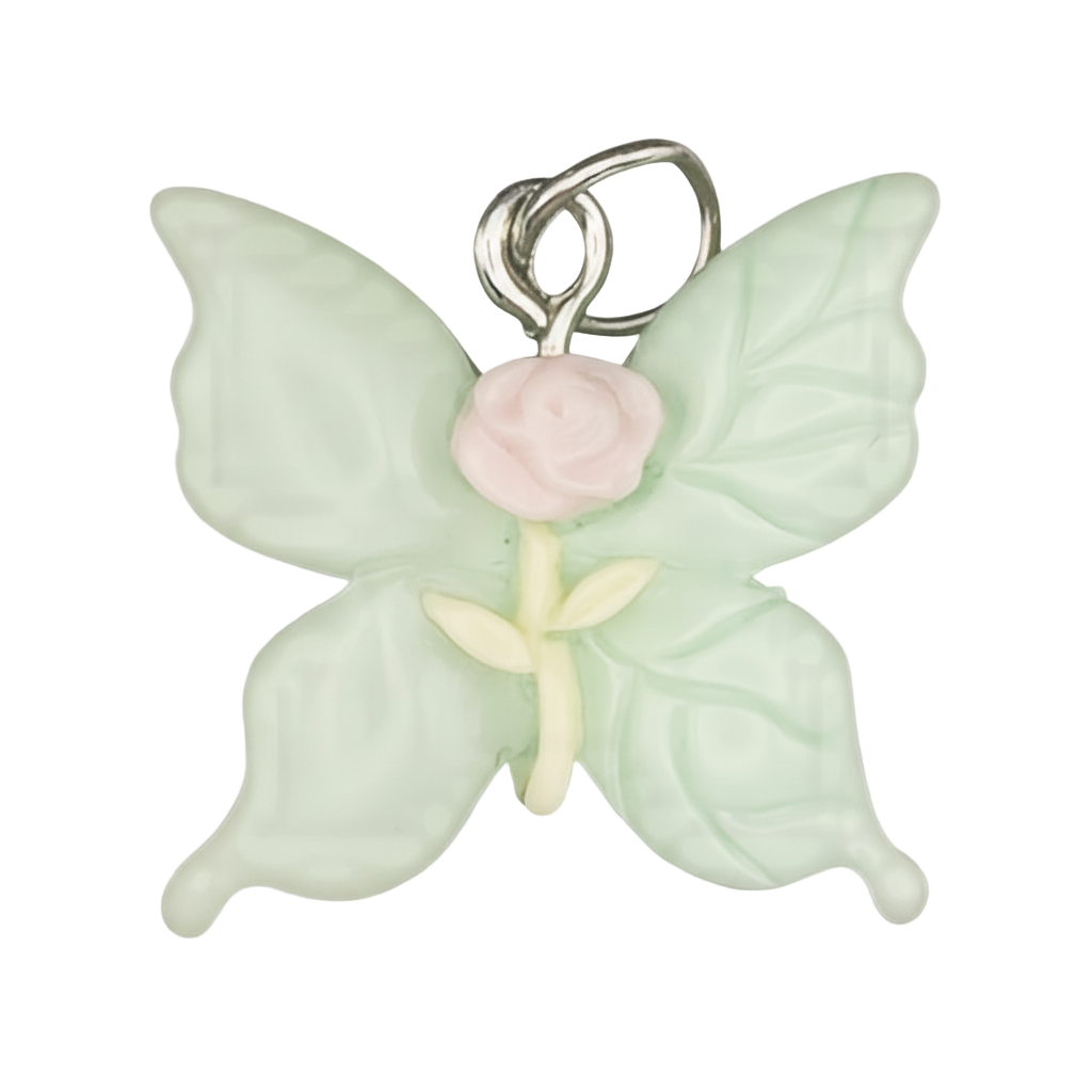 Close-up of mint green butterfly charm with a pink rose center on a black background.