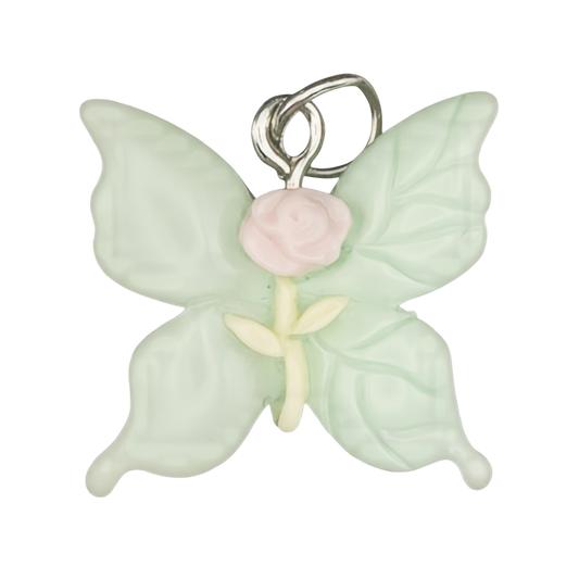 Close-up of mint green butterfly charm with a pink rose center on a black background.