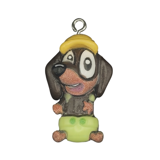 close-up of cartoon dog charm with yellow cap and green shorts on black background