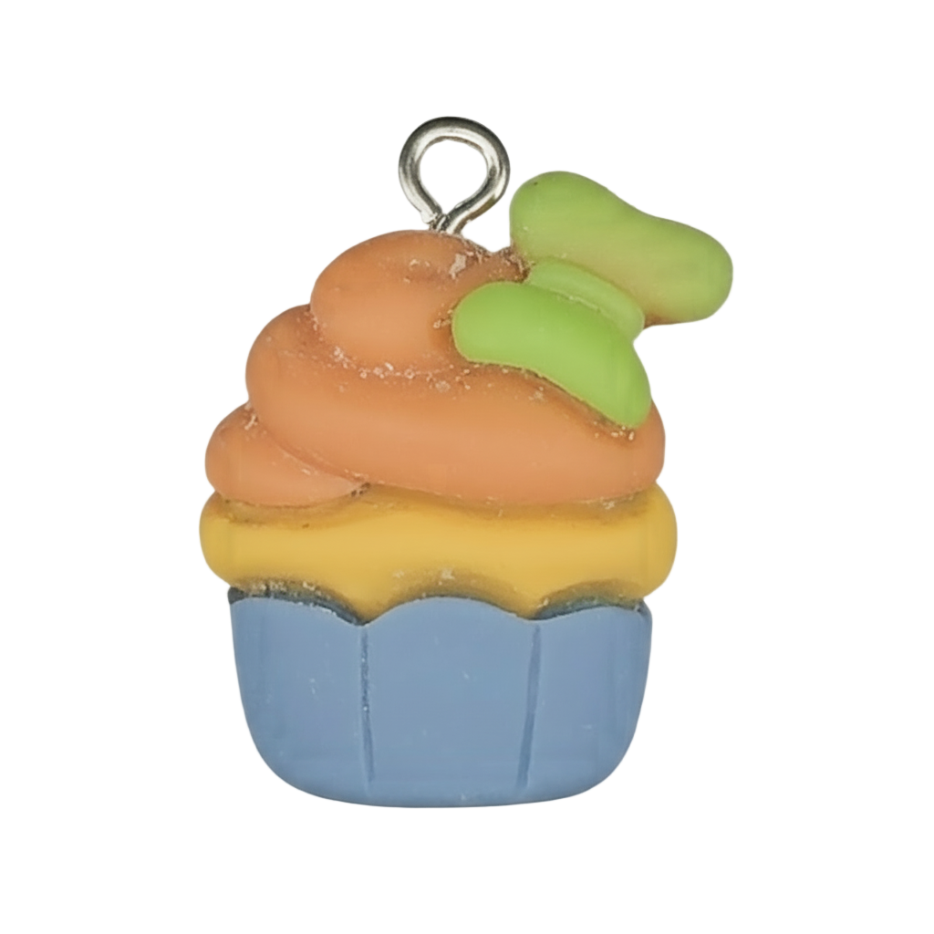 Close-up of a small cupcake charm with a blue cup, yellow layer, orange frosting, and a green accent on top against a black background.