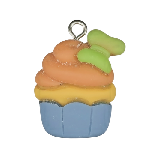 Close-up of a small cupcake charm with a blue cup, yellow layer, orange frosting, and a green accent on top against a black background.