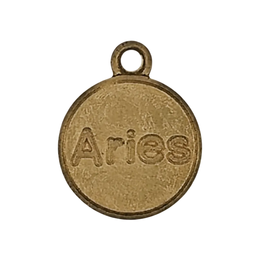 close-up of round gold-tone charm engraved with the word Aries on a black background