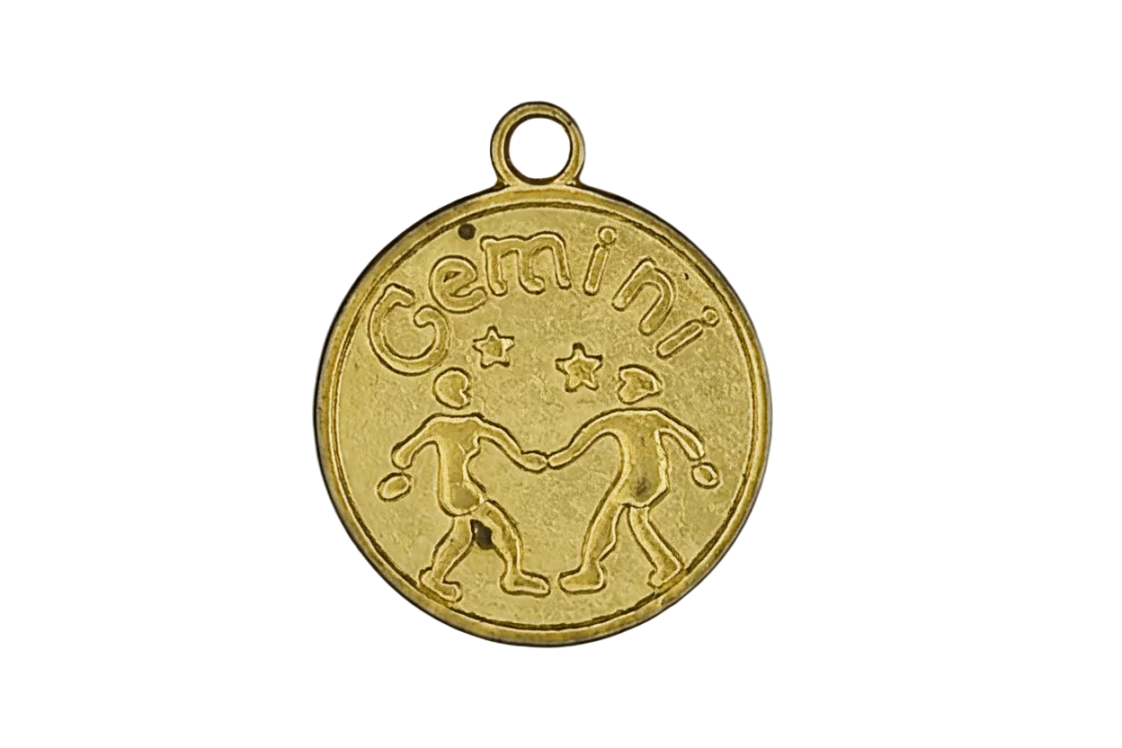 close-up of a gold round Gemini zodiac charm with twin figures and stars on a black background