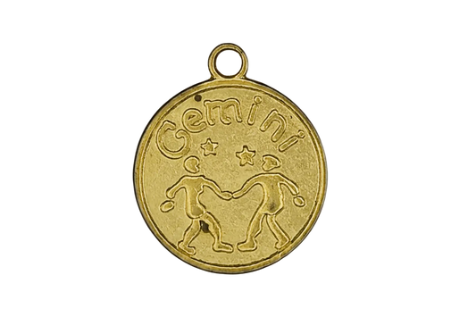 close-up of a gold round Gemini zodiac charm with twin figures and stars on a black background