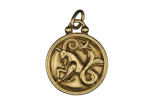 close-up of round gold-tone charm with raised unicorn, star, and scroll on black background