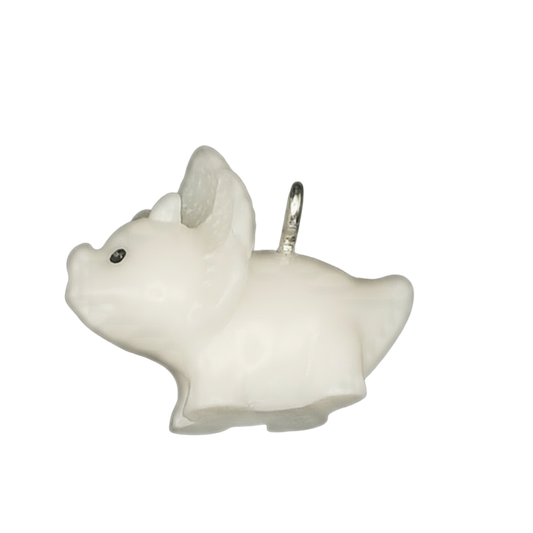 Close-up side view of a small white pig charm with black eye on a black background.