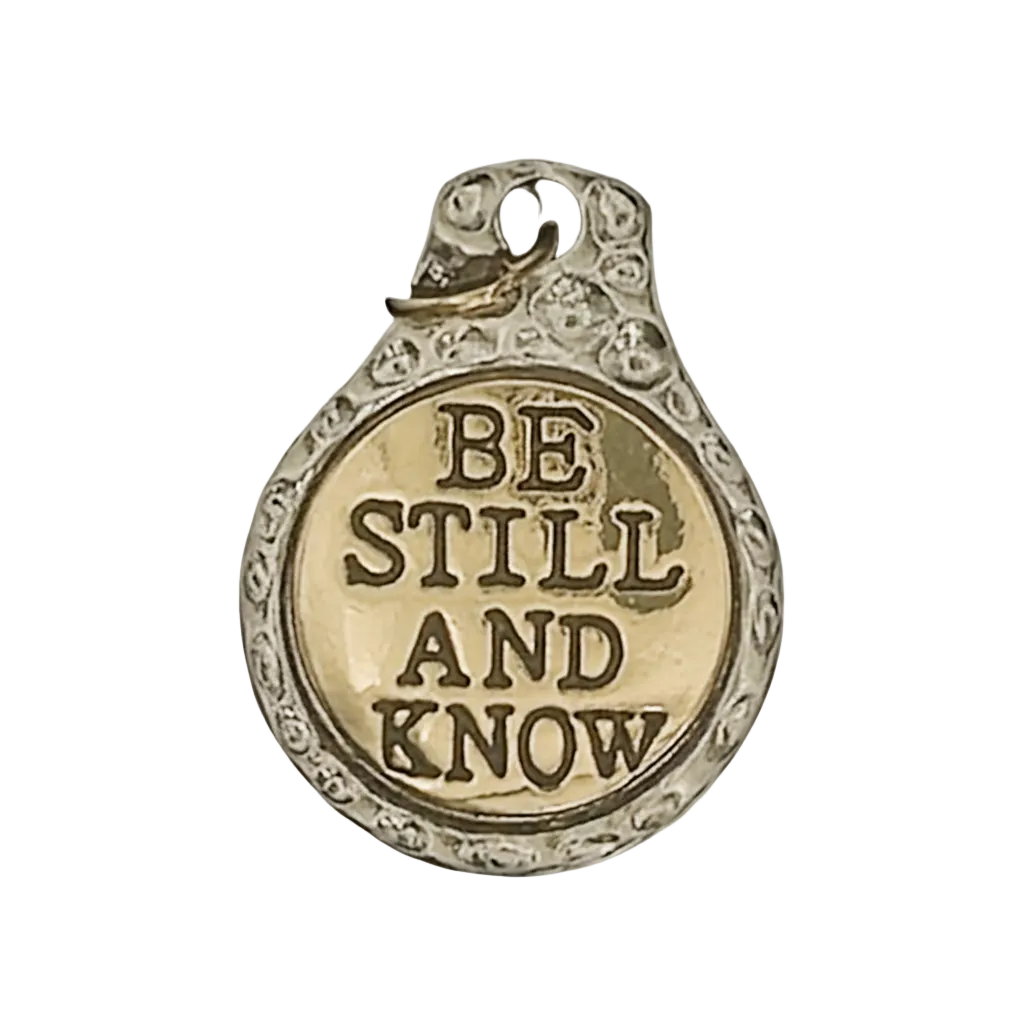 close-up of round two-tone charm reading BE STILL AND KNOW on black background