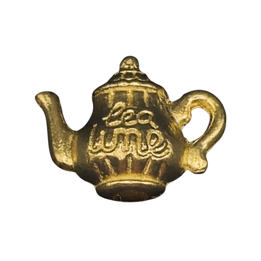 Close-up of an antique gold teapot charm with 'tea time' lettering on a black background.