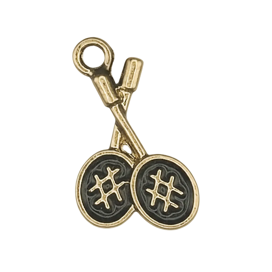Close-up of a gold-tone charm shaped like crossed knitting needles with two yarn balls on a black background.