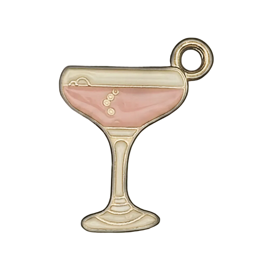 Close-up of a small enamel charm shaped like a coupe cocktail glass with pink drink and gold outline on black background.