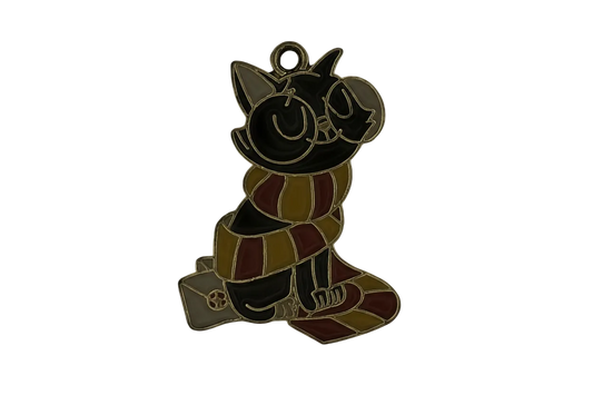Close-up of black enamel cat charm with red and yellow striped scarf and glasses, gold-tone outline, on a black background.
