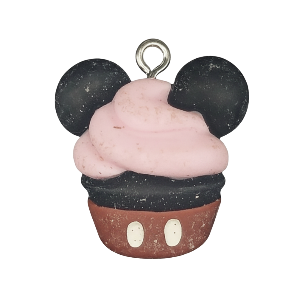 close-up of cupcake charm with mouse ears, pink frosting, and red base on a black background