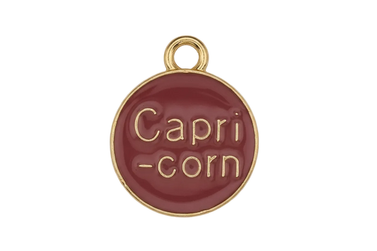 close-up of round red charm with gold 'Capri-corn' text on black background
