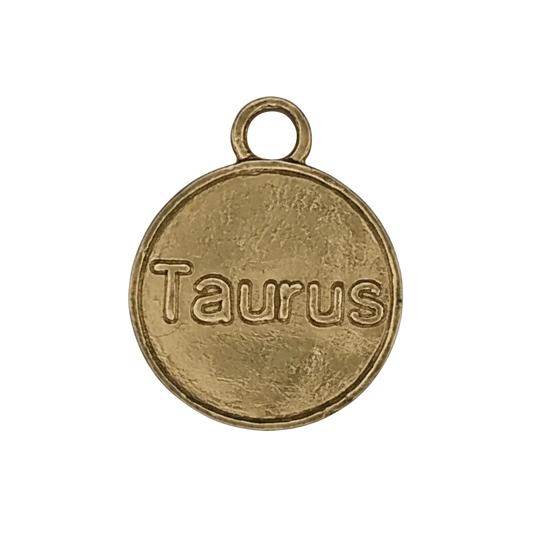 close-up of a round gold-tone charm engraved 'Taurus' with a small top ring on a black background