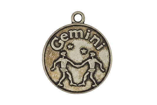 close-up of round Gemini zodiac charm with twin figures and stars in antique gold on black background